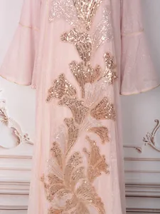 Détail en gros plan de la broderie florale de sequins dorés sur une robe rose