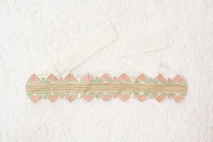 Vista detallada de un cinturón bordado étnico con patrones geométricos en rosa y oro