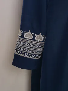 Gros plan de la broderie argentée complexe sur la manche d'une robe longue marine.