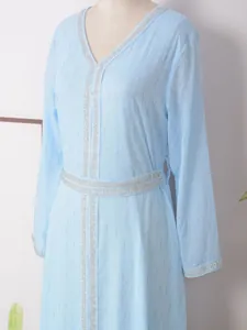 Détail d'une robe longue bleu clair à manches longues avec broderies de paillettes argentées