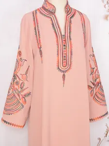 Detalle del bordado colorido en un vestido de manga larga rosa melocotón de moda.