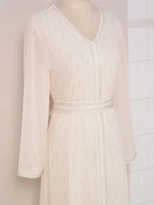 Vue détaillée d'une robe longue crème avec motifs dorés et une ceinture perlée élégante.