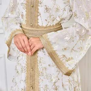 Gros plan sur l'imprimé floral doré et les galons d'un élégant caftan blanc chic