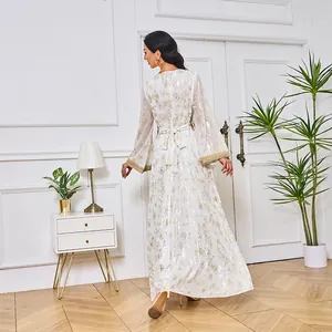 Robe longue Abaya blanche avec motif floral doré vue de dos dans un décor intérieur.