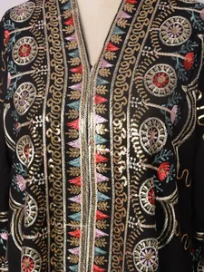 Nahaufnahme aufwendiger bunter Stickereien und goldener Pailletten auf schwarzem Kleid.