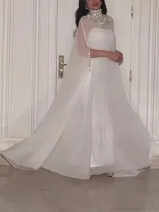 Detail van een witte maxi-jurk met een glinsterende pailletten cape en een hoge kraag.