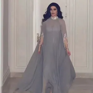 Elegante lichtgrijze maxi-jurk met pailletten cape en split detail, getoond door een model binnen