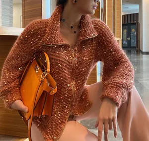 Dettaglio ravvicinato di un maglione in maglia ruggine con paillettes dorate e zip frontale
