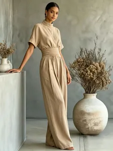 Full-length view of a beige short sleeve wide-leg jumpsuit in a minimalist setting