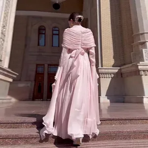 Elegant pink pleated maxi dress featuring a bow detail and flowing sleeves in a grand setting