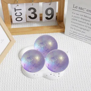 Gros plan de trois balles anti-stress à paillettes violettes sur un plateau en nuage