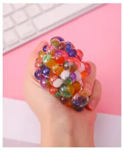 Close-up of a hand squeezing a colorful mesh grape stress ball with water beads