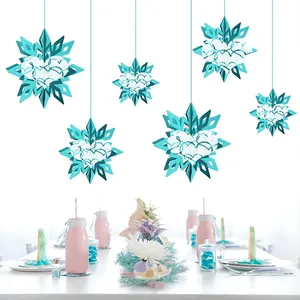 Six teal 3D paper snowflake ornaments hanging above a decorated party dining table