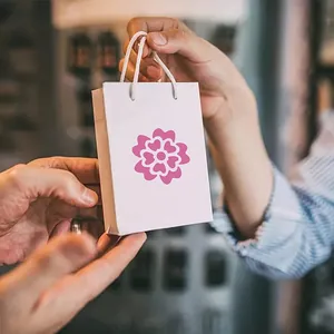 Petit sac cadeau en papier blanc avec motif floral rose tenu par des mains en magasin
