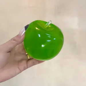Detail einer Hand, die ein grünes, transparentes Antistress-Spielzeug in Apfelform hält.