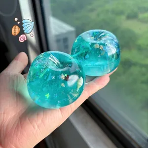 Close-up of a translucent turquoise apple squishy toy with sparkling ocean shell glitter