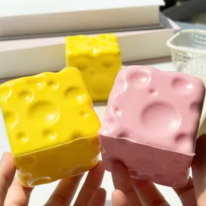 Vue détaillée de jouets squishy en forme de fromage jaune et rose tenus dans la main.