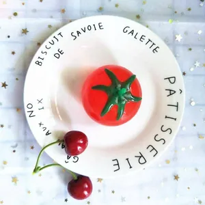 Detalle superior de una bola antiestrés con forma de tomate rojo en un plato blanco.