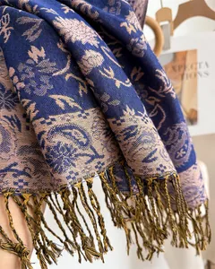 Detailed view of the intricate blue and beige paisley pattern on a soft cashmere-like fringed scarf
