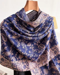 Detailed view of a blue and tan paisley pashmina shawl hanging on a wooden hanger.