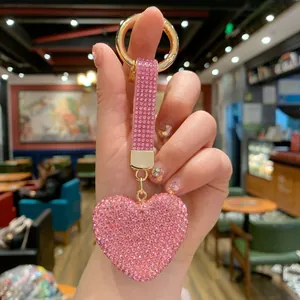 Close-up of a pink heart keychain with glittering rhinestones held by a manicured hand