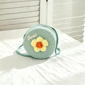 Detailed view of a girl's mint green straw woven bag featuring a yellow crochet flower