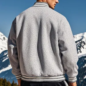 Detail view of a men's gray textured fleece varsity jacket against a snowy mountain.