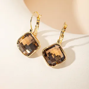 Gros plan de boucles d'oreilles carrées en or avec pierres facettées champagne.