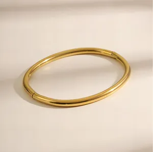 Detail van een minimalistische gepolijste gouden ovale armband met veilige scharniersluiting.