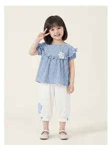 Little girl wearing a blue plaid ruffled top and white pants set for the summer season