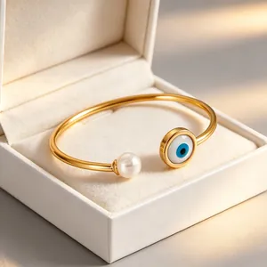 Dettaglio ravvicinato di un bracciale in acciaio dorato con occhio greco e perla