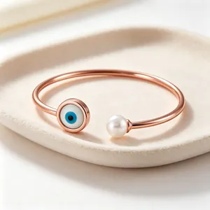 Dettaglio di un bracciale in oro rosa con occhio di Allah e perla su vassoio crema.