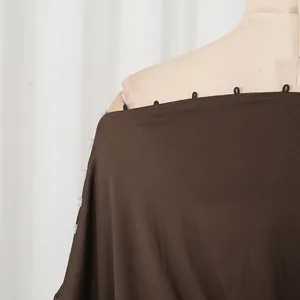 Dettaglio ravvicinato del top marrone con spalle scoperte e rifiniture di asole e bottoni chic.