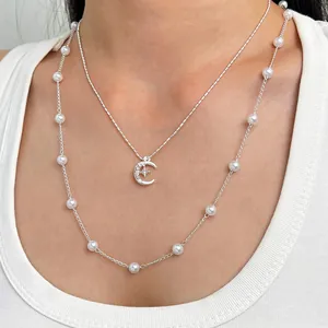 Elegante collana a doppio strato con pendente luna e stella e dettagli in perle bianche.