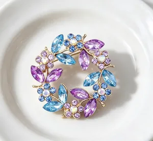 Macro view of vintage floral wreath brooch with purple and blue crystals on white plate