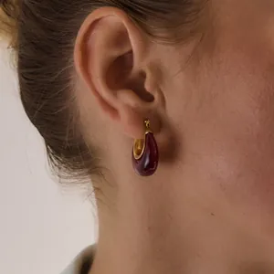 Close-up detail of a burgundy resin teardrop hoop earring worn by a female model