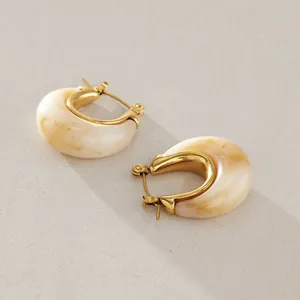 Detail view of minimalist gold-plated titanium steel hoop earrings with cream marbled resin
