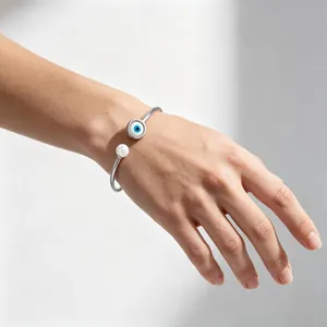 Dettaglio di bracciale in acciaio con occhio di Allah e perla su polso femminile