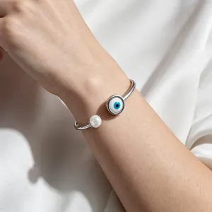 Dettaglio ravvicinato del bracciale rigido in acciaio inox con occhio blu e perla sul polso