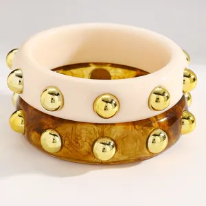 Close-up detail view of vintage acrylic bangles with gold studs in cream and amber