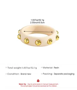Detailed macro view of retro cream-colored resin bangle with gold-colored studded spheres