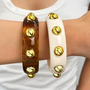 Close-up of stacked retro chunky acrylic bangles in amber and cream with gold studs.