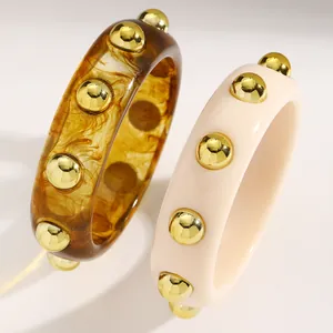 Macro detail of acrylic bangles with embedded golden metallic studs in amber and cream.