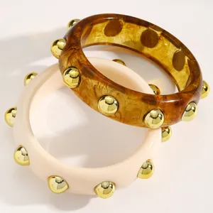 Detail view of chunky retro acrylic bangles with gold studs in amber and cream