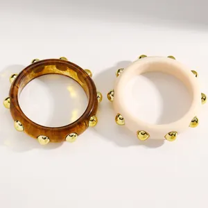Detail view of wide acrylic bangles with polished gold-tone metal stud embellishments.
