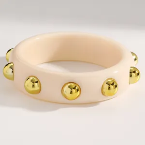 Detailed close-up of a cream acrylic wide bangle with decorative gold sphere studs