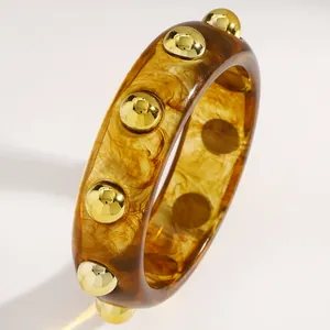 Macro detail of a vintage amber acrylic bangle featuring polished gold metal studs