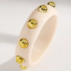 Close-up detail of a cream retro acrylic wide bangle featuring gold metallic dot studs