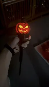 Detailed view of a glowing solar Halloween pumpkin stake light held in hand at night