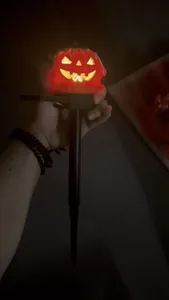 Glowing solar-powered Halloween Jack-O'-Lantern stake light held in hand at night